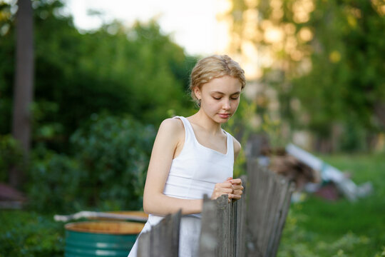 Girl in a white dress standing by a fence outdoors in a serene setting