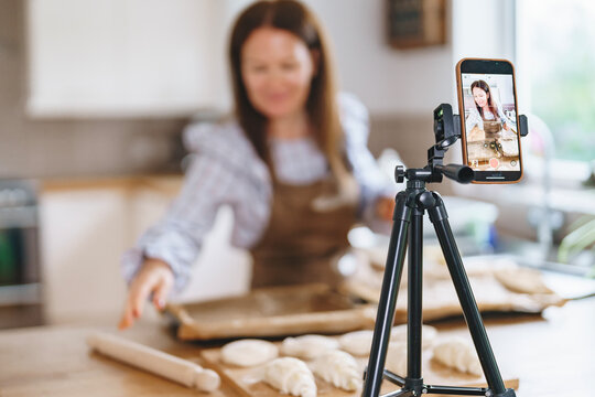 Baking activity in a bright kitchen featuring a woman filming her process with a smartphone on a tripod while preparing dough for pastries