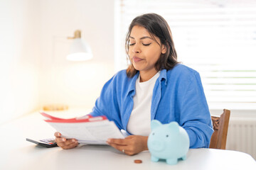 Sad Woman reviewing financial documents at home with a piggy bank and calculator on a sunny day