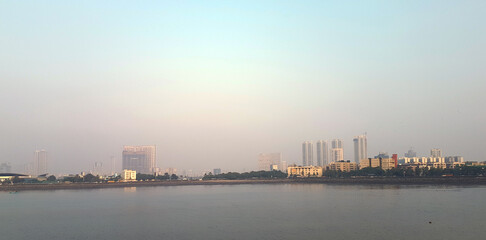 Obraz premium Early morning light casts a calm glow over the Mumbai skyline, showcasing modern buildings and tranquil water below