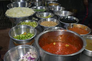 Various bowls filled with fresh vegetables, sauces, and spices are arranged in a kitchen, showcasing a vibrant cooking setup at twilight