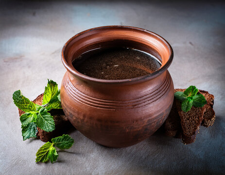 A rustic clay pot filled with Latvian rupjmaize (dark rye bread) kvass surrounded by sprigs of fresh mint.