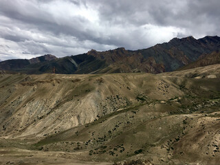 A breathtaking view of Leh Ladakh reveals expansive hills and dramatic mountain ranges, all under a dynamic cloud-filled sky