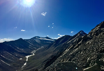 Expansive view of Leh Ladakh features rugged mountains, a gentle river, and bright sunlight illuminating the landscape