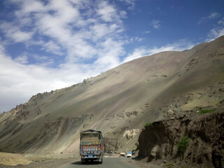 Journey along a winding road in Leh Ladakh with towering mountains and clear skies, capturing the beauty of this remote region