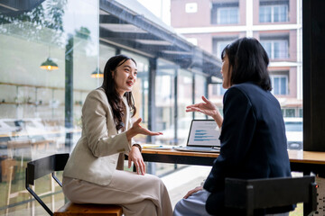 Fototapeta premium Two women are sitting at a table, one of them is talking to the other