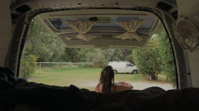 Rear view of a young woman drapes a towel outside her camper van after a refreshing shower,