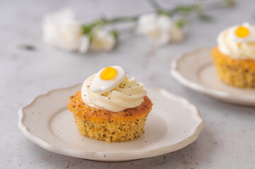 Lemon Poppy Seed Cupcakes with lemon curd and cream cheese topping and Fried Egg candies. Colourful Easter eggs, flowers on a stone background, top view. Easter holiday and festive food.