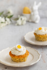 Lemon Poppy Seed Cupcakes with lemon curd and cream cheese topping and Fried Egg candies. Colourful Easter eggs, flowers on a stone background, top view. Easter holiday and festive food.