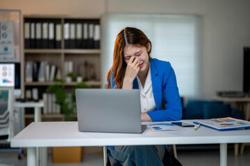 A woman is sitting at a desk with a laptop and a stack of papers