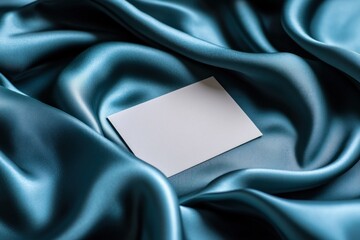 A blank business card rests on soft blue satin fabric, ideal for showcasing design and branding creativity in a sleek setting
