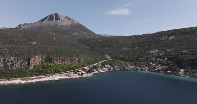 Aerial forward of Limeni, Greece along the coast with large mountain in background on a sunny spring morning in the Peloponeese.