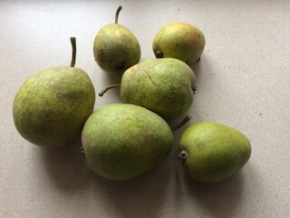 Six ripe green pears on a light beige surface displaying natural freshness
