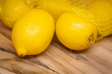 Fresh yellow lemons in a mesh bag on a rustic wooden surface. Healthy eating, zero waste, eco...