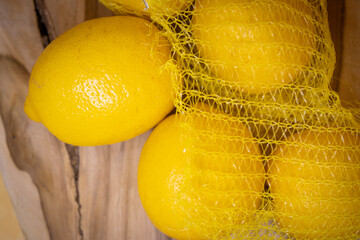 Fresh yellow lemons in a mesh bag on a rustic wooden surface. Healthy eating, zero waste, eco...