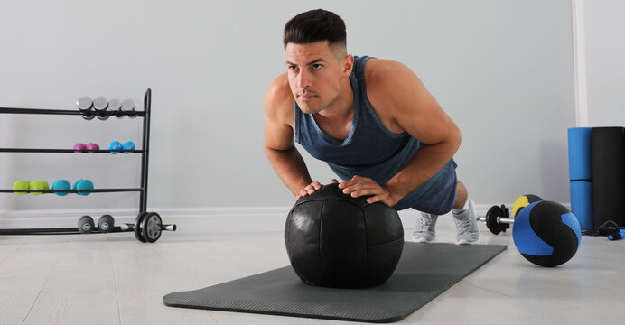 Athletic man doing push ups with medicine ball in modern gym, space for text