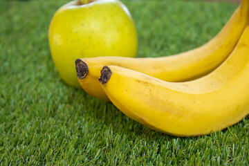 Bananas and an apple placed on green grass. Healthy eating, natural food, fresh fruit, organic,...