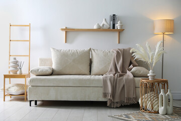 Comfortable sofa with pillows, blanket, lamp and different decor near white wall indoors. Interior design