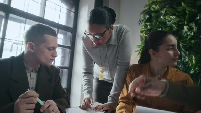 Zoom in shot of young inspired diverse coworking team collaborating together at one table during brainstorm meeting in modern green office