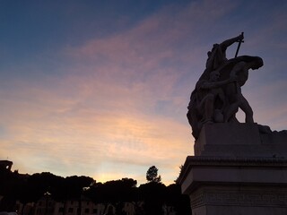 Obraz premium Ancient statue in Rome set against a sunset sky painted in soft pink hues. Perfect for themes of history, art, and romantic travel moments.