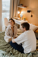 Obraz premium In a cozy room, a White woman about 30 years old sits on the bed and looks to the side, and her White husband sits in front of her. The concept of thoughtfulness, a day off, a heart-to-heart talk.
