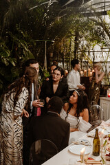 Group of diverse adults at an elegant indoor wedding reception. A Black bride in a white gown sits beside the groom as guests stand nearby conversing.