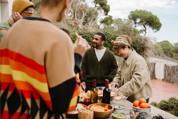 A multinational group of adult people is preparing food for dinner together outdoors in a cozy...