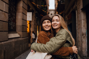 Two fair-skinned female friends are hugging and standing on a narrow city street on a cloudy day. The concept of meeting a friend, walking around the city, the joy of friendship.