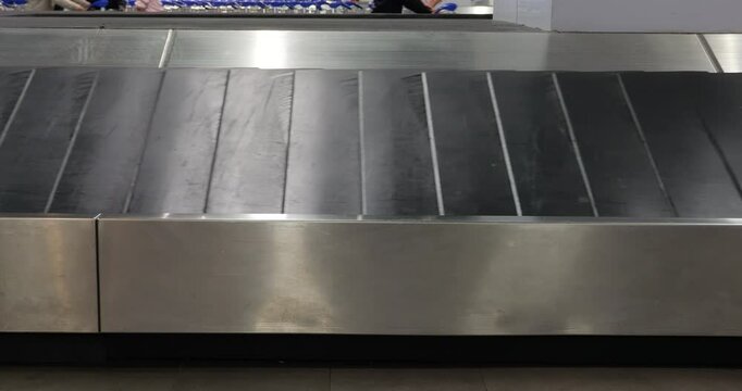 Medium shot of empty luggage carousel in international airport. One black bag slides along at conveyor belt. Typical scene of the baggage claim area. Someone did not pick up their bag after arrival.