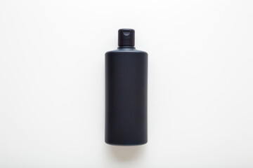 Dark black plastic shampoo or shower gel bottle on light gray table background. Care about clean and soft body skin. Beauty product. Closeup. Top down view.