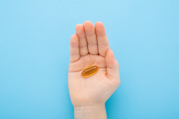 Little child boy palm holding and showing fish oil capsule or d vitamin on light blue table...