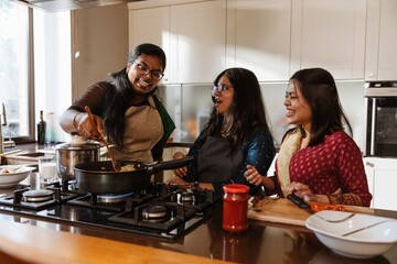 An Indian woman in her 30s stirs food in a frying pan while demonstrating the cooking process to...