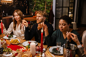 An overweight African American woman in her late 30s, sitting among a White family at the dinner table in their cozy home, praying with them during the Christmas dinner