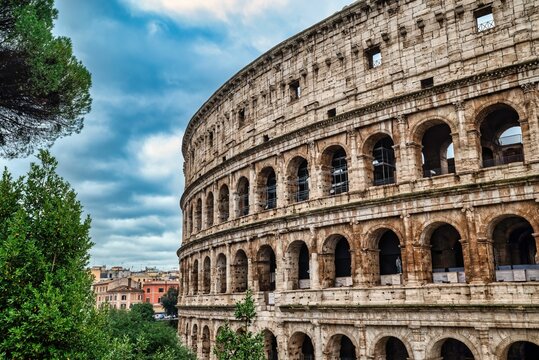 The Colosseum in Rome with lush greenery and a cloudy sky.