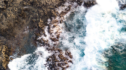 Drone point of view of Atlantic ocean waves meet with underwater pointed rocky. Blue rough sea with big waves with foam crashing against the rocks, south of Tenerife, Canary island