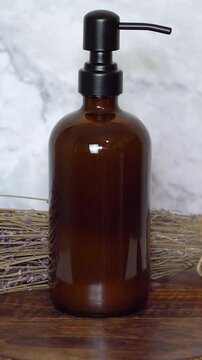 Amber glass shampoo bottle with dry lavender flowers on dark wooden board and marble background. Natural beauty flat lay with rustic, eco-friendly, and calming herbal haircare elements.