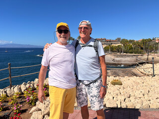 Happy couple of senior men friends in excursion along the sea looking at camera smiling, two elderly pensioner males enjoying healthy lifestyle in outdoors