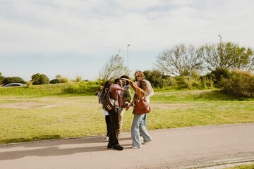 Obraz premium A group of five young friends in their late 20s, hugging and greeting each other as they meet on a walkway in a lush park, on a sunny day, all smiling cheerfully