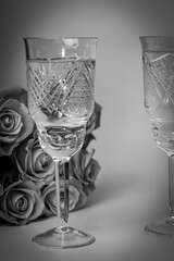 Black and white vertical photo of two glasses and roses on a light background, romantic setting, side view