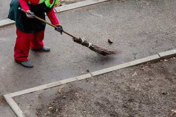 Sweeping the asphalt path, a janitor with a broom in bright workwear is at work. His labor symbolizes care for order in public areas and maintaining cleanliness in the city.
