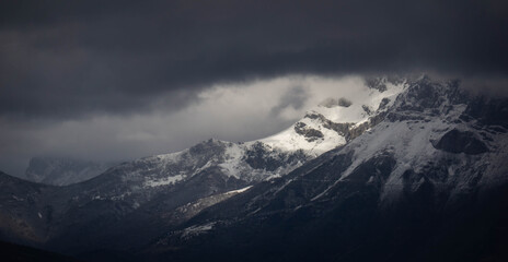 Cloudy and mysterious day in the mountains with the sun shining to the snowy hill through dark clouds