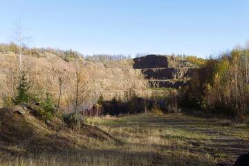 Borówno Mine, Poland - a landscape featuring a former quarry with exposed rock faces, a body of water at the bottom, and surrounding autumn foliage under a clear sky