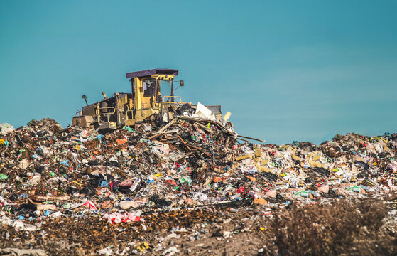 Bulldozer working on a large landfill full of mixed waste and garbage under clear blue sky.