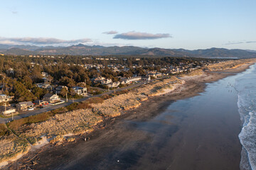 Aerial drone picture of Manzanita Beach on the Oregon Coast, showing waves of the Pacific Ocean, small coastal town, sunset, sandy shoreline, forested mountains. Perfect for travel and tourism themes © Hrach