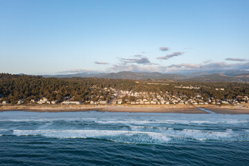Aerial drone picture of Manzanita Beach on the Oregon Coast, showing waves of the Pacific Ocean, small coastal town, sunset, sandy shoreline, forested mountains. Perfect for travel and tourism themes © Hrach