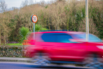 A red car is driving fast on a road with a speed limit of 50 km, the car is blurred in motion