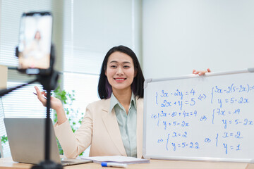 Education session featuring a smiling Asian woman teaching mathematics online in a bright room with...