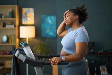 Woman holding her forehead while exercising on treadmill, surrounded by modern decor. Light from...