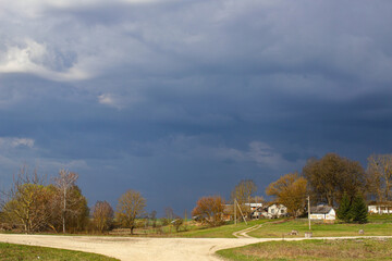 Dramatic cloudy sky before a thunderstorm over a peaceful Ukrainian village. Storm clouds, green grass, bare trees in early spring. Stormy sky over village