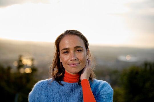Woman in blue sweater and red turtleneck outside with sunset background
